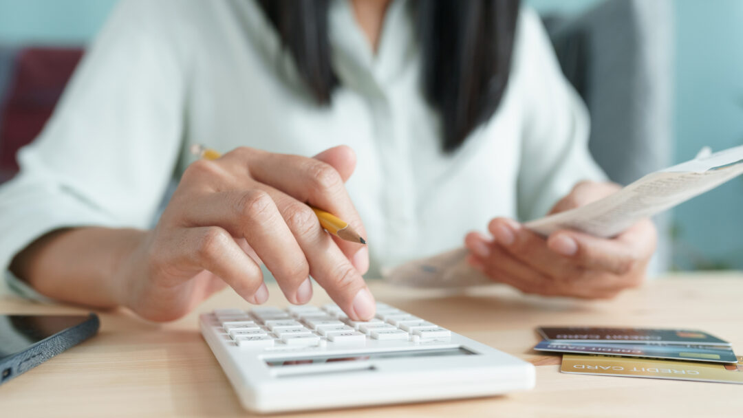 Person using a calculator while holding a bill, with credit cards on the table.