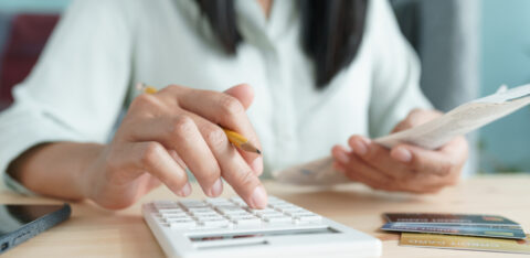 Person using a calculator while holding a bill, with credit cards on the table.
