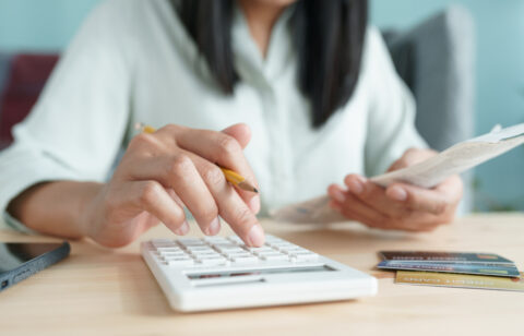 Person using a calculator while holding a bill, with credit cards on the table.