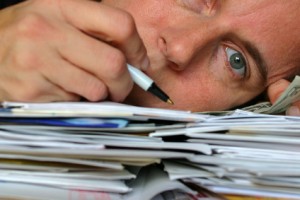 Man with pen in hand peering over stack of bills and looking for debt relief