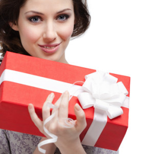 Young woman holds a gift wrapped in red paper, isolated on white
