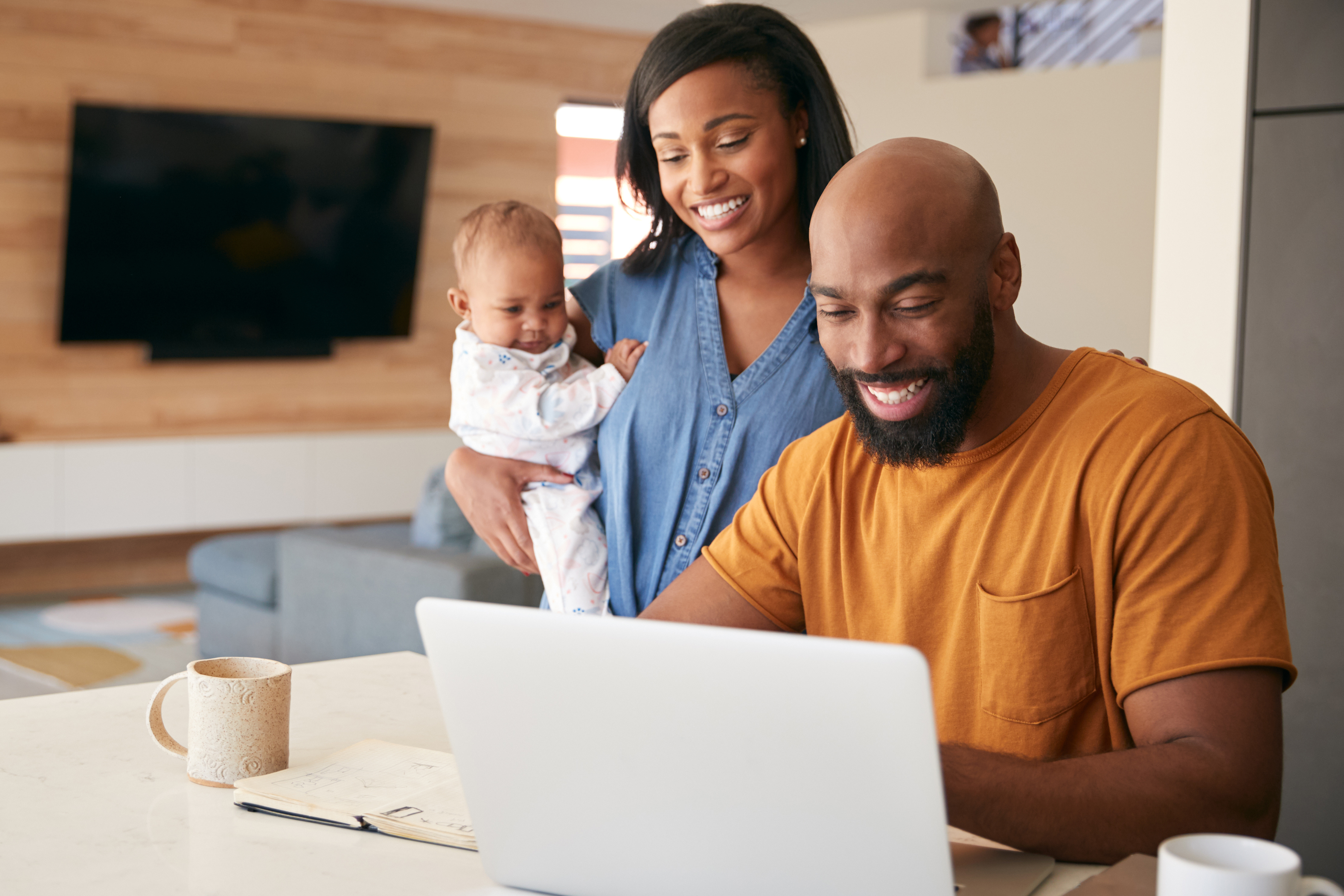 Smiling parents with their baby looking at a laptop together in the kitchen.