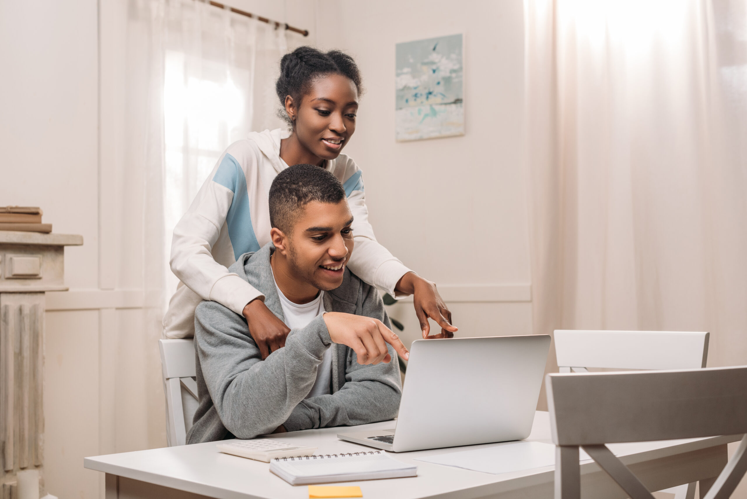 happy african american couple using laptop and pointing on screen at home