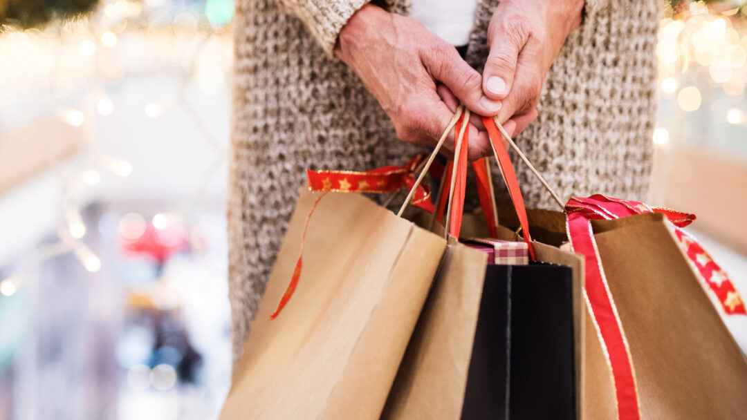 Older adult holding several holiday shopping bags in a mall.