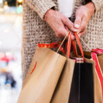 Older adult holding several holiday shopping bags in a mall.
