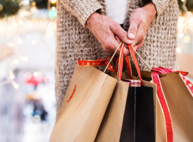 Older adult holding several holiday shopping bags in a mall.