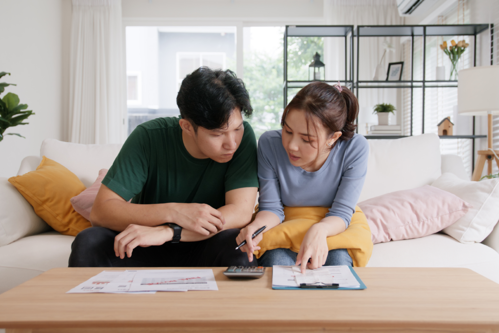 Young partners budgeting together on the couch with paperwork and a clipboard.