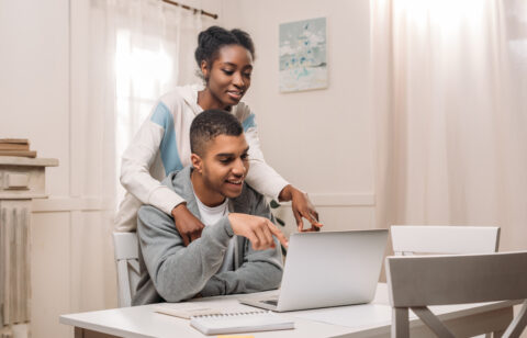 happy african american couple using laptop and pointing on screen at home