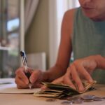 Woman managing a tight budget by counting cash and recording expenses at a kitchen table.