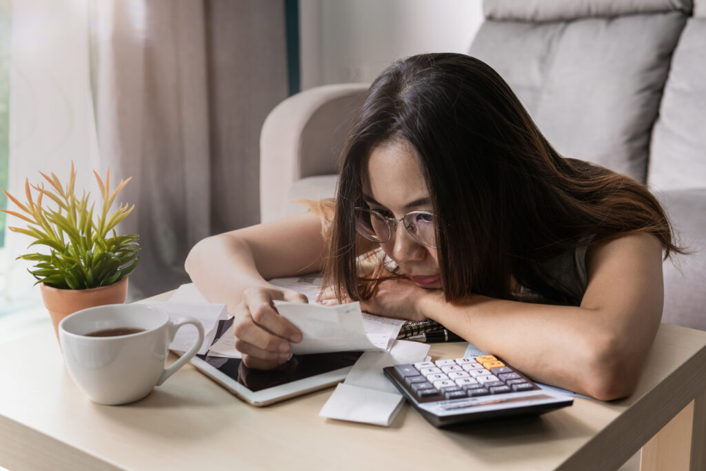 Woman wearing glasses reviewing receipts and financial documents at a table with a calculator and tablet.