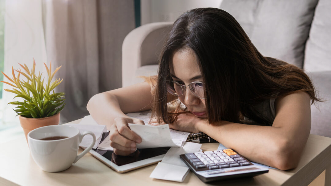 Woman wearing glasses reviewing receipts and financial documents at a table with a calculator and tablet.