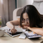 Woman wearing glasses reviewing receipts and financial documents at a table with a calculator and tablet.