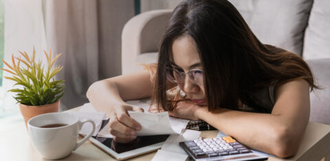 Woman wearing glasses reviewing receipts and financial documents at a table with a calculator and tablet.