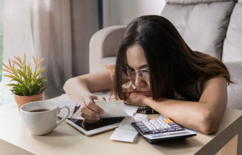 Woman wearing glasses reviewing receipts and financial documents at a table with a calculator and tablet.