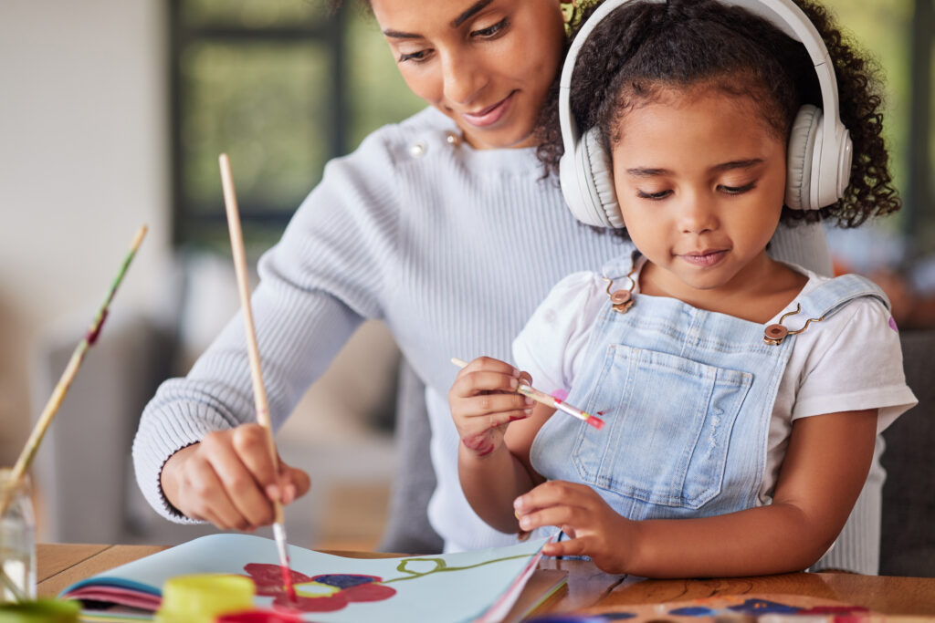 Mother and daughter painting together at home, with the child wearing headphones while creating artwork.
