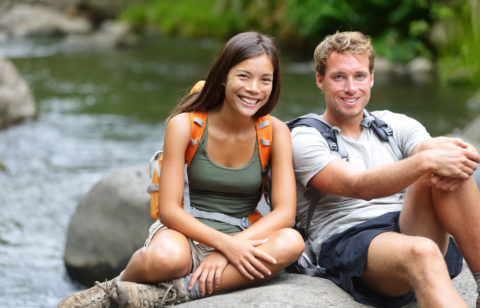 A hiking couple rest by a river while out on a date.