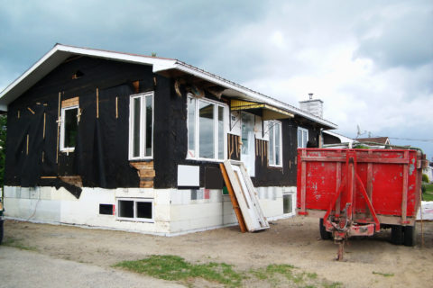 A fixer-upper being worked on, with its siding removed and a dumpster out front.
