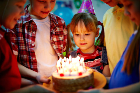 A small circle of children holding up a birthday cake for one to blow out the candles.