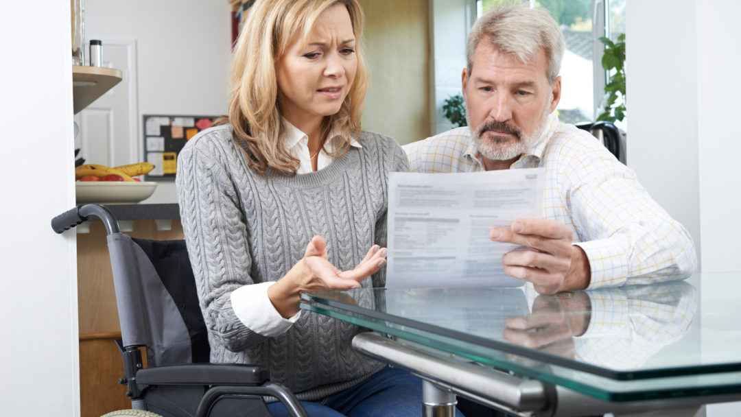 A frustrated couple — one seated in a wheelchair — looking over a medical bill.