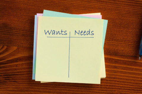 A piece of paper has a line drawn down the middle, splitting the words “wants” and “needs” written at the top.