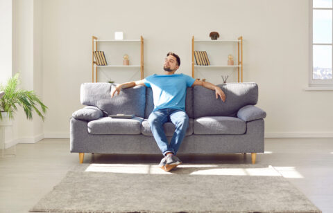 Relaxed young man is enjoying free time and sitting on comfortable couch at home