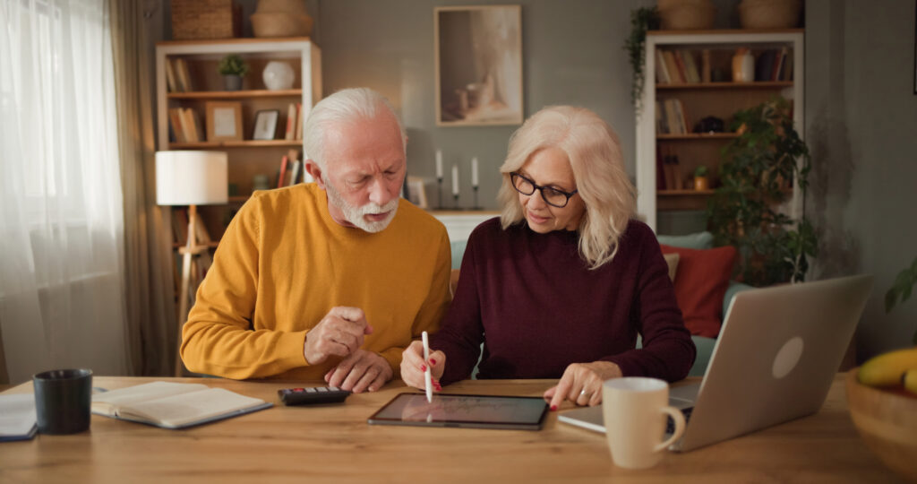 Retired couple reviewing financial information together on a tablet while working through household finances at home.