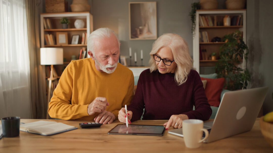 Retired couple reviewing financial information together on a tablet while working through household finances at home.