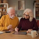 Retired couple reviewing financial information together on a tablet while working through household finances at home.