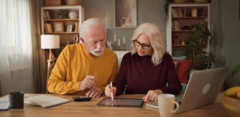 Retired couple reviewing financial information together on a tablet while working through household finances at home.