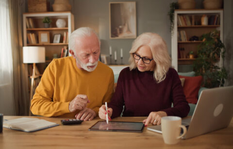 Retired couple reviewing financial information together on a tablet while working through household finances at home.