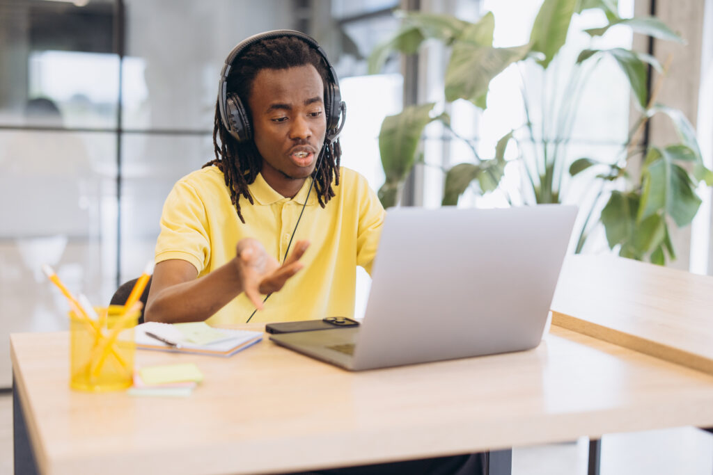African american man having a virtual meeting on a laptop, working remotely with headphones in a modern office