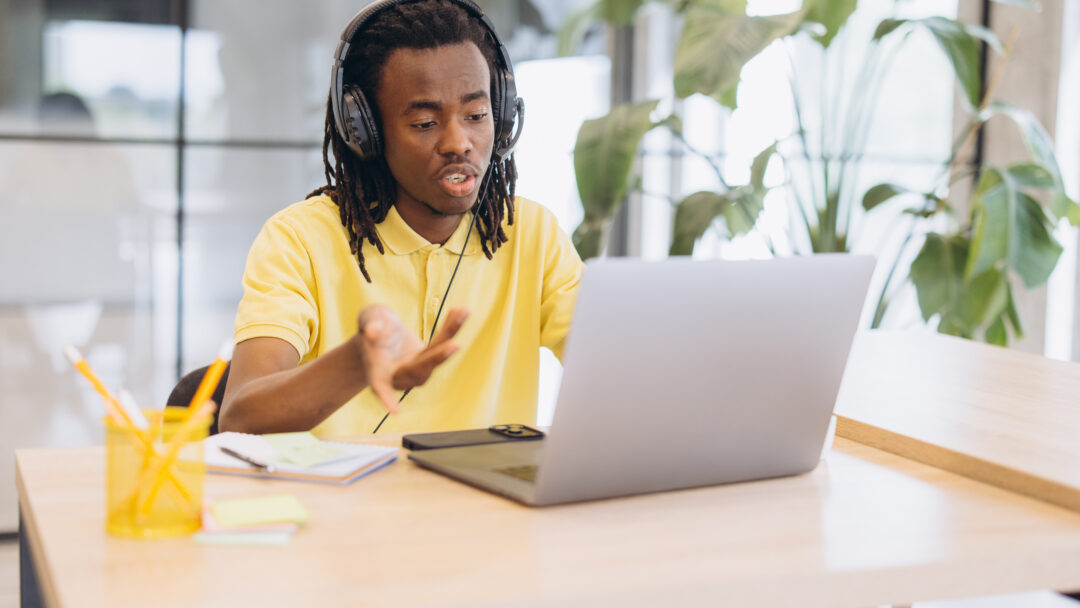 African american man having a virtual meeting on a laptop, working remotely with headphones in a modern office