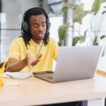 African american man having a virtual meeting on a laptop, working remotely with headphones in a modern office