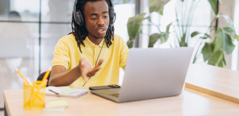African american man having a virtual meeting on a laptop, working remotely with headphones in a modern office