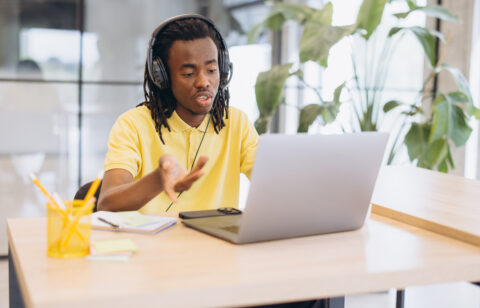 African american man having a virtual meeting on a laptop, working remotely with headphones in a modern office