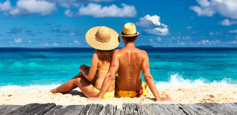 A couple on their honeymoon sitting on a tropical beach in their swimsuits.