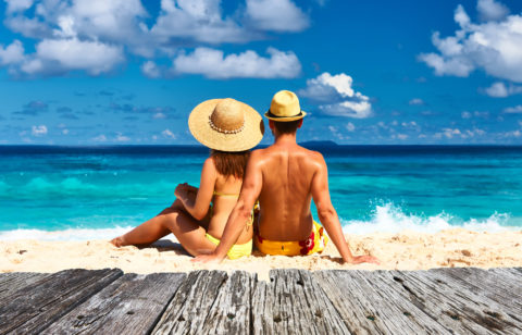 A couple on their honeymoon sitting on a tropical beach in their swimsuits.