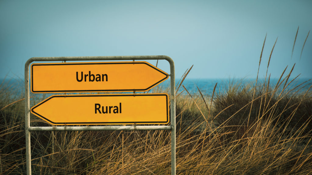 A directional sign by a lake points two ways — left for “rural,” and right for “urban.”