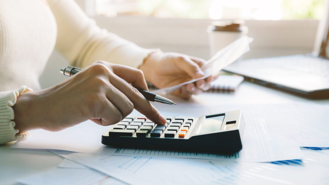 Woman managing her budget by reviewing bills, calculating expenses, and organizing financial documents at home.