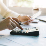 Woman managing her budget by reviewing bills, calculating expenses, and organizing financial documents at home.