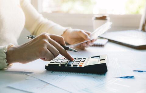 Woman managing her budget by reviewing bills, calculating expenses, and organizing financial documents at home.