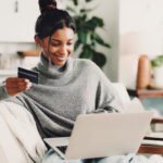 Home, laptop and woman on sofa, credit card and digital app for online banking. Ecommerce, pc and happy person on couch, electronic transaction or payment for website subscription, smile and fintech