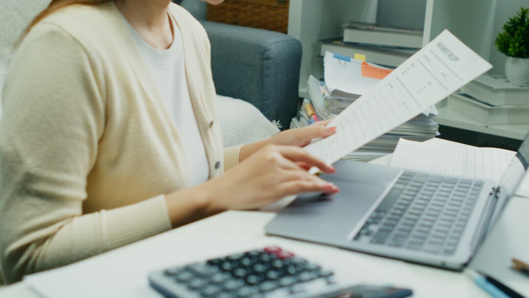 Individual Reviewing Financial Reports.An Asian individual reviews financial reports and property rates, calculating income and expenses with serious dedication using technology.