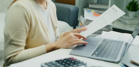 Individual Reviewing Financial Reports.An Asian individual reviews financial reports and property rates, calculating income and expenses with serious dedication using technology.