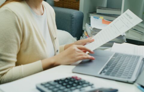 Individual Reviewing Financial Reports.An Asian individual reviews financial reports and property rates, calculating income and expenses with serious dedication using technology.