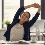 Woman stretching at her desk in an office while taking a break from working on her computer.