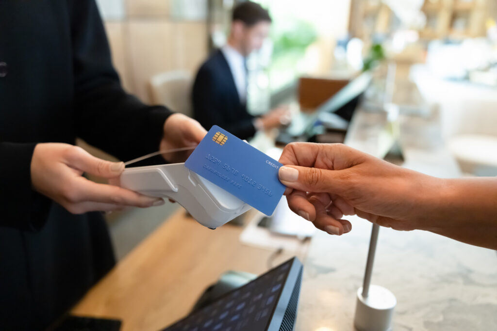 A customer holds a blue credit card near a contactless payment terminal at a checkout counter.