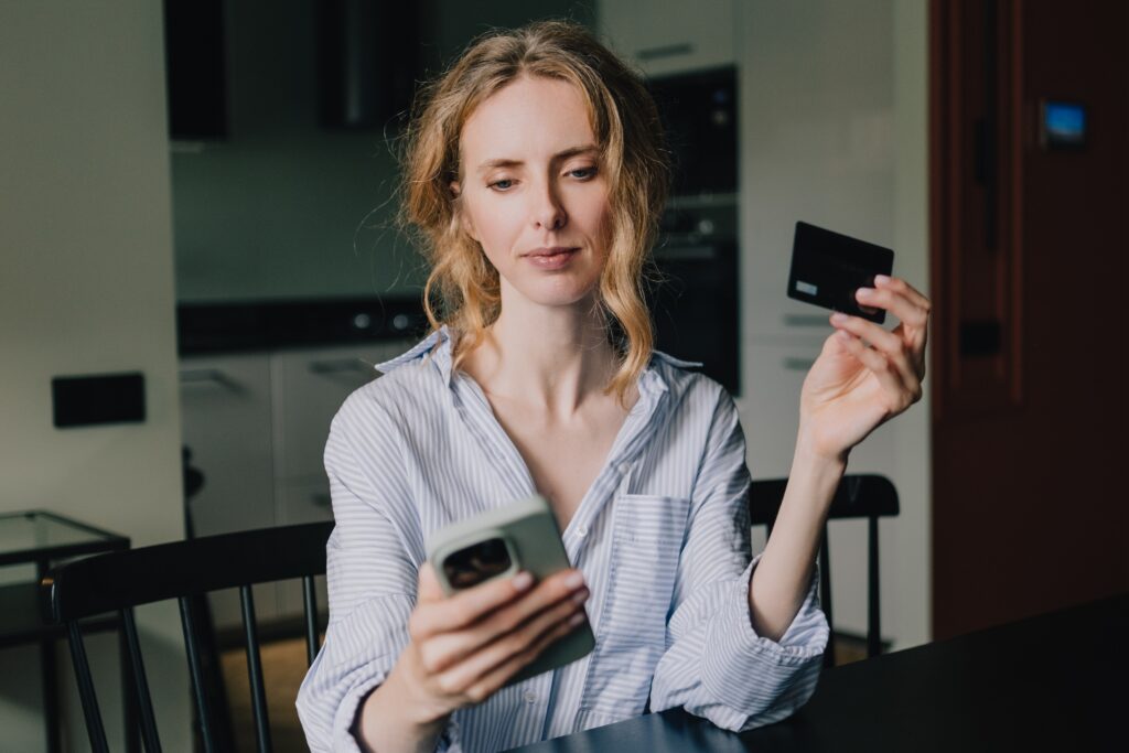 A woman holds a credit card while looking at her smartphone at home.