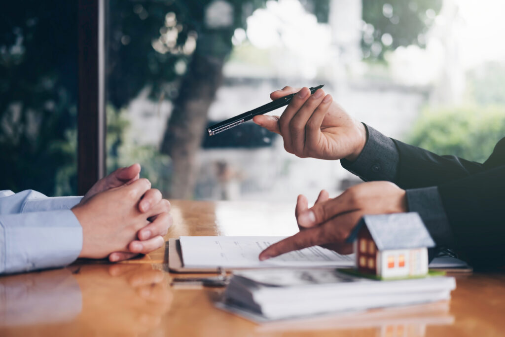 Financial professional discussing paperwork with a client at a desk with a small model house in the foreground.