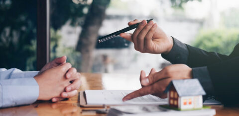 Financial professional discussing paperwork with a client at a desk with a small model house in the foreground.